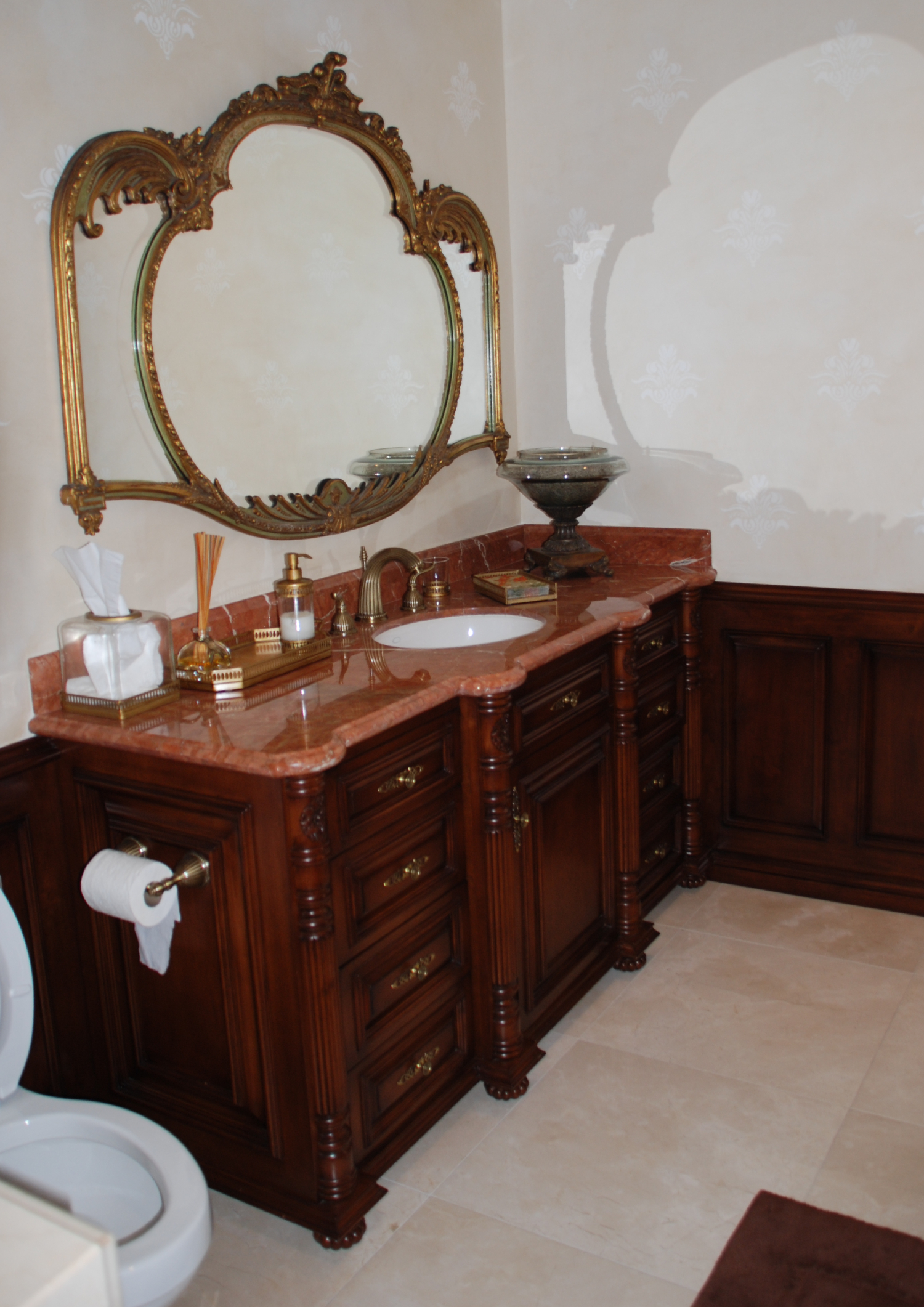 Baño elegante con mueble de madera oscura, encimera de mármol y detalles dorados.